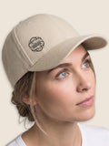 Woman wearing a stone Scottish Malt Whisky Society baseball cap with black logo on the front right panel.