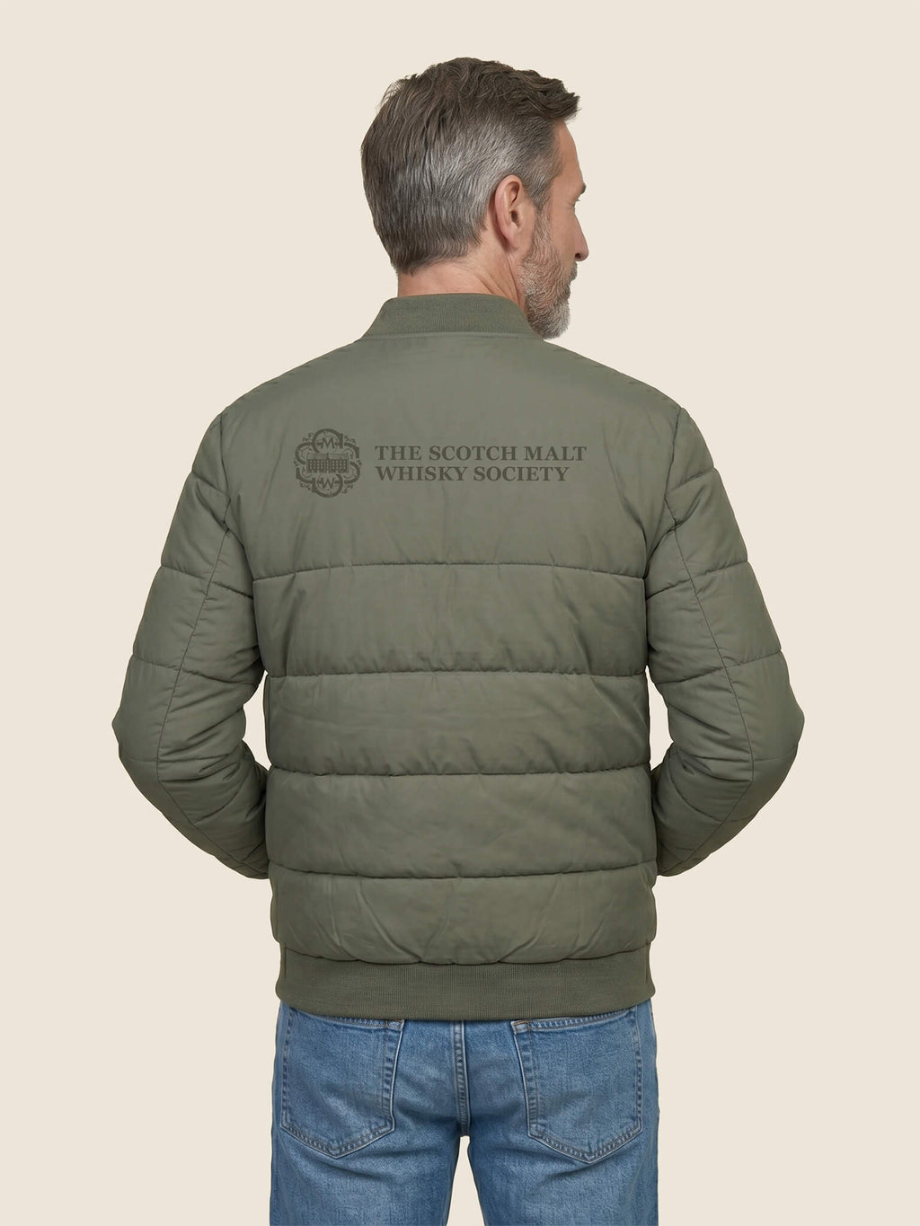 Side view of man wearing a khaki Scottish Malt Whisky Society padded jacket with tone on tone logo across the shoulders.