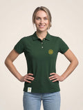 Woman wearing forest green fitted polo shirt with gold SMWS logomark on the left chest.