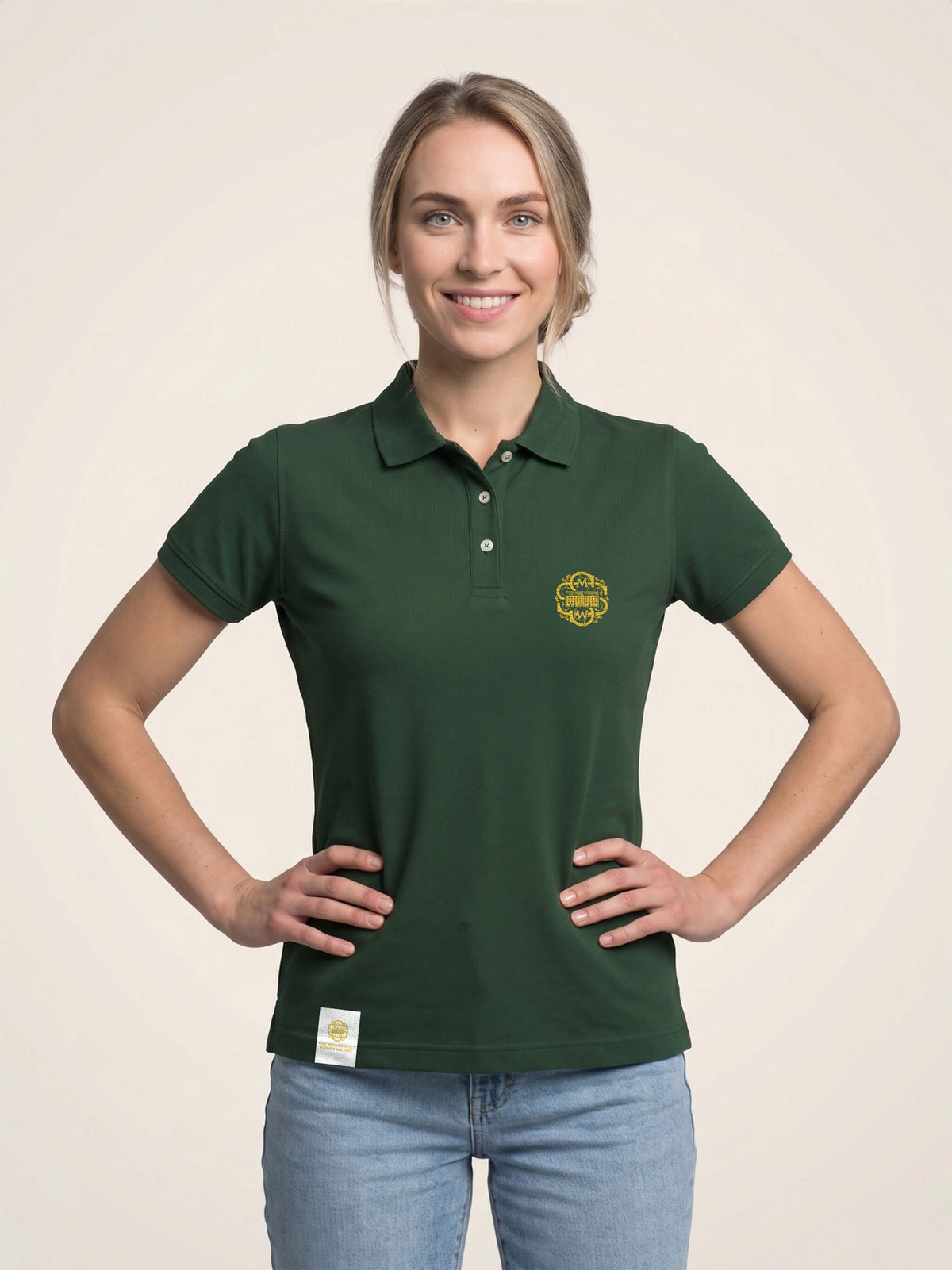 Woman wearing forest green fitted polo shirt with gold SMWS logomark on the left chest.
