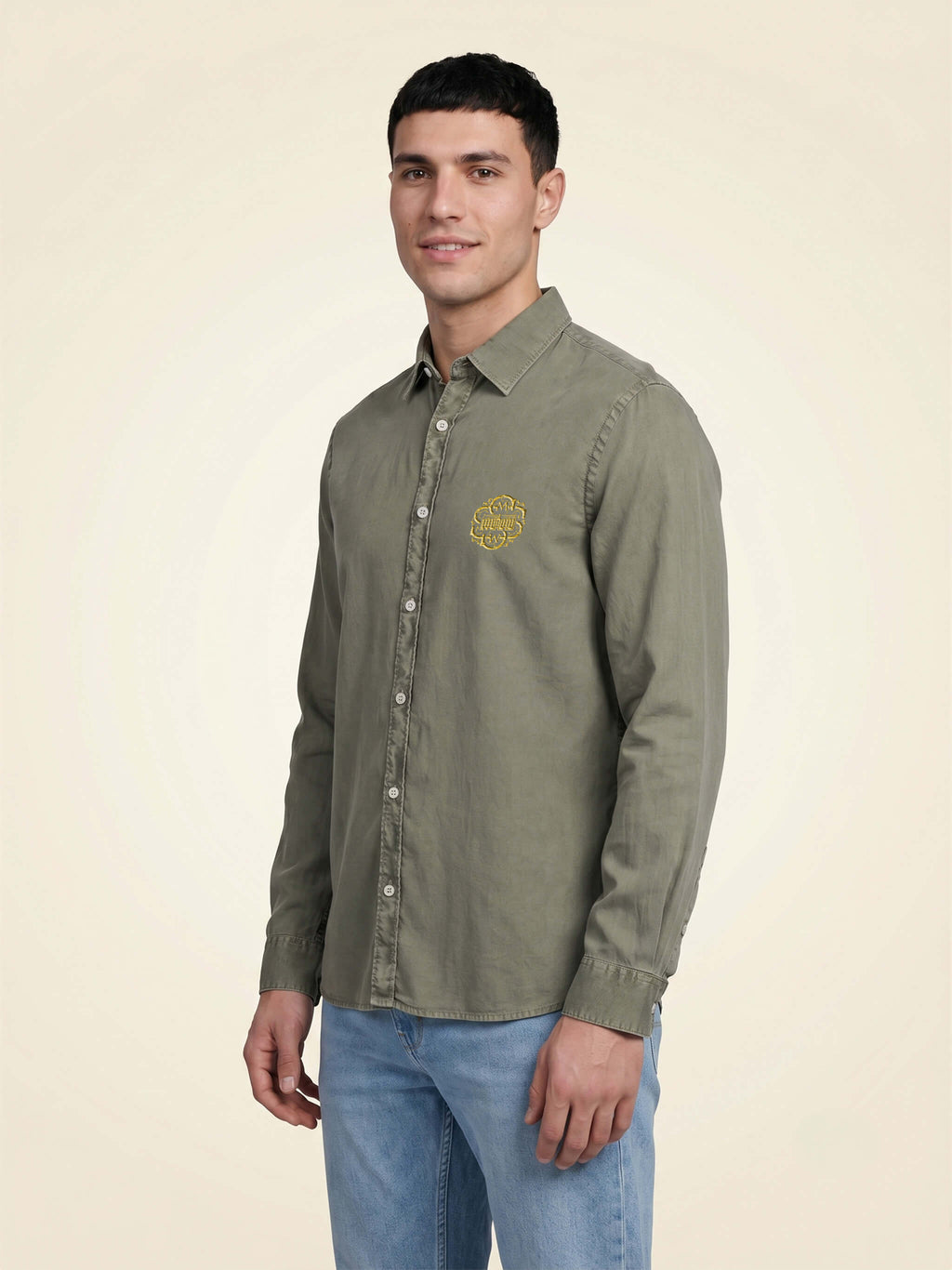 Side view of man wearing a washed pale Khaki organic cotton shirt with SMWS logo mark on left chest. 