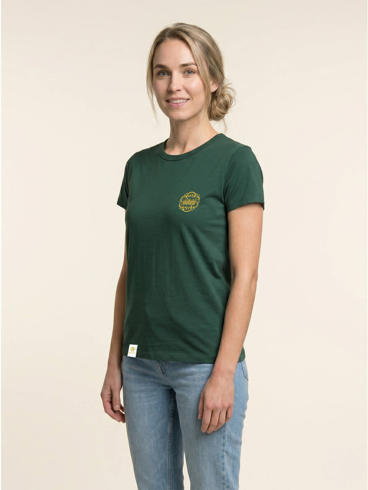 Side view of woman wearing a forest green Scottish Malt Whisky Society t-shirt with gold logo on the left chest.