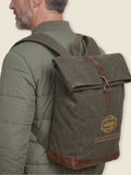 Man wearing Scottish Malt  Whisky Society olive green, waxed roll top backpack with gold logo on the front panel